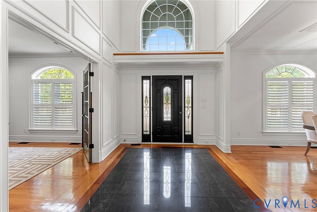 Two-story foyer at 13446 Bradley Bridge Road, with a Palladian arch window above the front door, dark stone and hardwood flooring, and white wainscoting