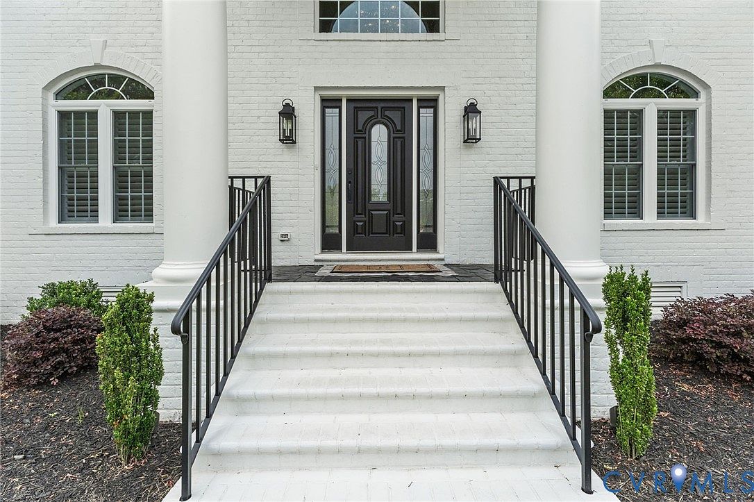 Close approach to the front entry: white painted brick columns, a leaded glass dark wood door flanked by tall sidelights, lanterns at shoulder height, and clipped boxwoods at the base of each column