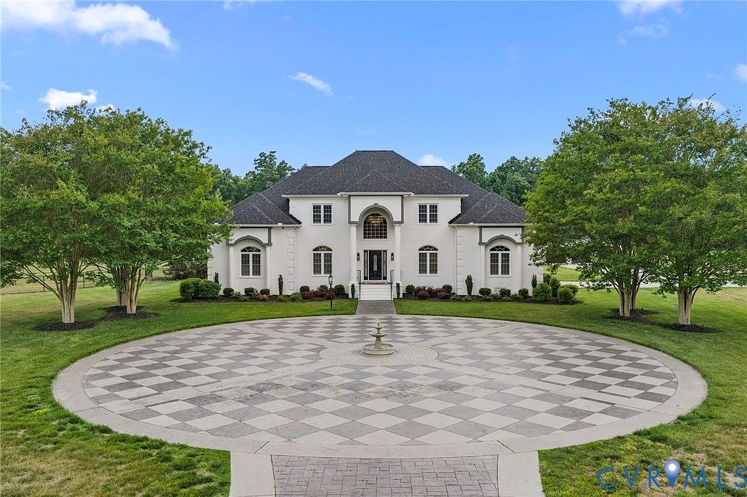 Front elevation of 13446 Bradley Bridge Road, a two-story white-painted brick French Provincial estate centered behind a circular driveway with a stone fountain, framed by mature crepe myrtles